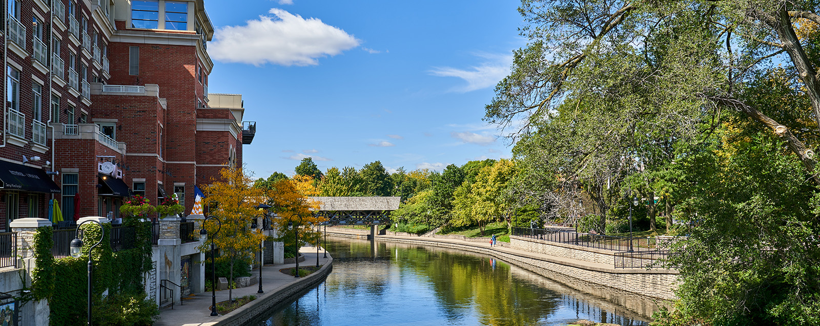 The image depicts a serene river scene with a bridge, houses, and trees in the background.