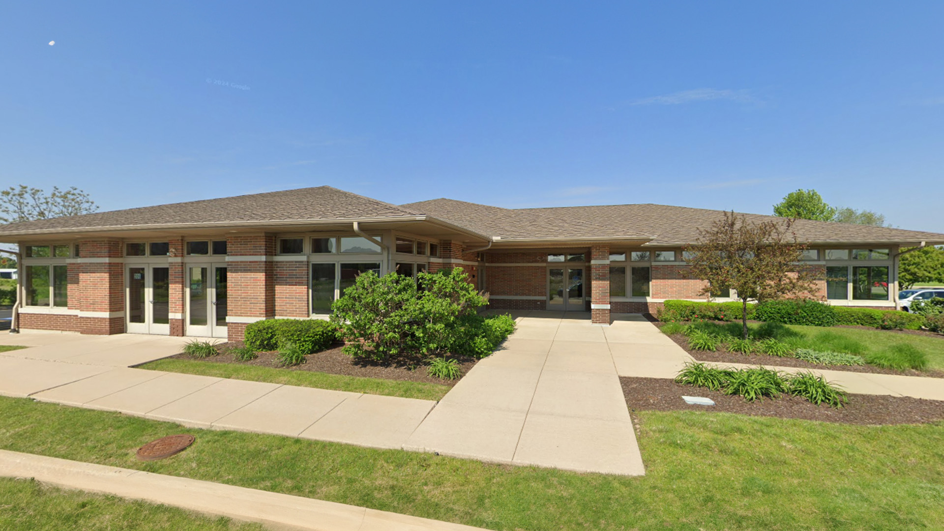 The image shows a two-story building with a flat roof, featuring a prominent entrance with a canopy supported by columns and a series of windows along the front facade.